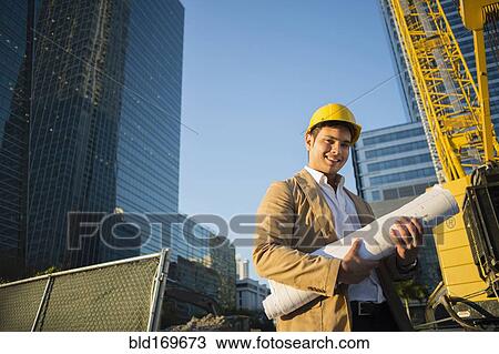 Stock Image - Mixed race architect holding blueprints at construction site. Fotosearch