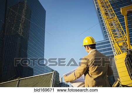 Stock Image - Mixed race architect reading blueprints at construction site. Fotosearch