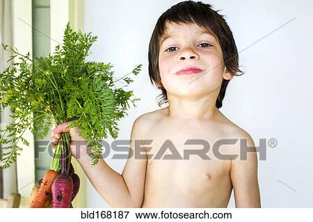 Stock Photo - Mixed race boy holding fresh picked carrots. Fotosearch