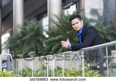 Stock Image - Mixed race businessman leaning on banister. Fotosearch