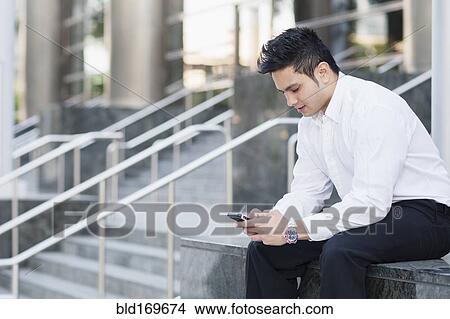 Picture - Mixed race businessman using cell phone near staircase. Fotosearch