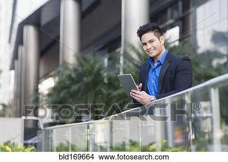 Picture - Mixed race businessman using digital tablet outdoors. Fotosearch