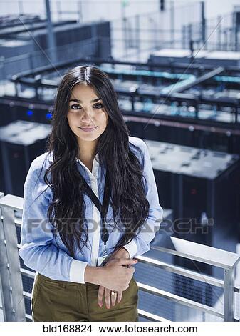 Picture - Mixed race businesswoman smiling on balcony over server room. Fotosearch