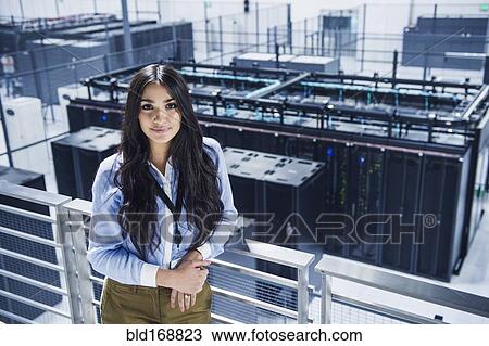 Stock Image - Mixed race businesswoman smiling on balcony over server room. Fotosearch