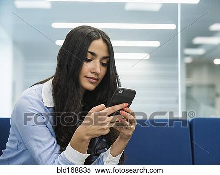 Stock Photography - Mixed race businesswoman using cell phone in office lobby. Fotosearch