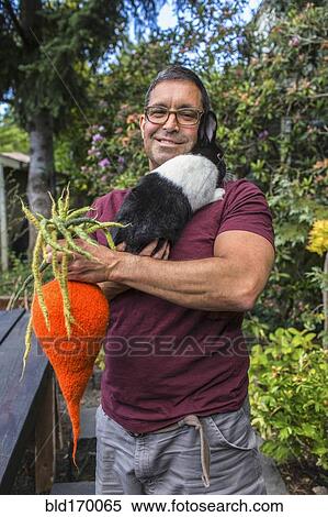 Stock Photography - Mixed race man carrying rabbit and knitted carrot. Fotosearch