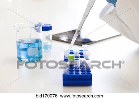 Stock Photograph - Mixed race scientist pipetting liquid into test tubes in laboratory. Fotosearch