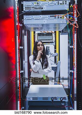 Stock Image - Mixed race technician examining computer in server room. Fotosearch