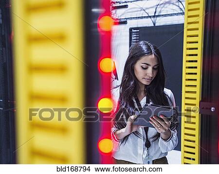 Picture - Mixed race technician using digital tablet in server room. Fotosearch