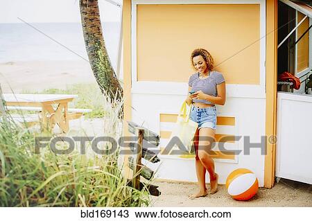Stock Image - Mixed race teenager using cell phone on beach. Fotosearch