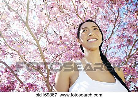 Stock Photo - Mixed race woman standing under flowering tree. Fotosearch