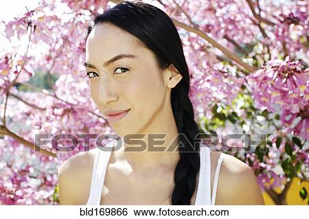 Stock Photograph - Mixed race woman standing under flowering tree. Fotosearch