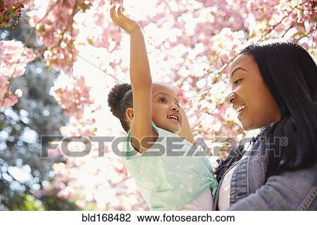 Stock Image - Mother and daughter under flowering tree in park. Fotosearch