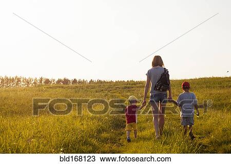 Stock Image - Mother and sons walking in rural field. Fotosearch