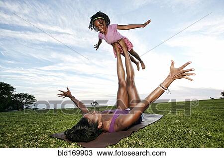 Stock Image - Mother balancing daughter on legs in park. Fotosearch