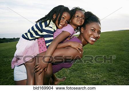 Picture - Mother carrying children piggyback in park. Fotosearch