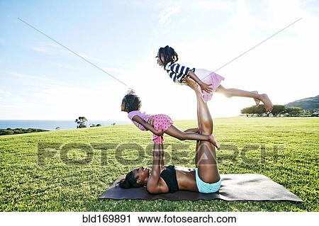 Stock Image - Mother holding children on yoga mat in park. Fotosearch