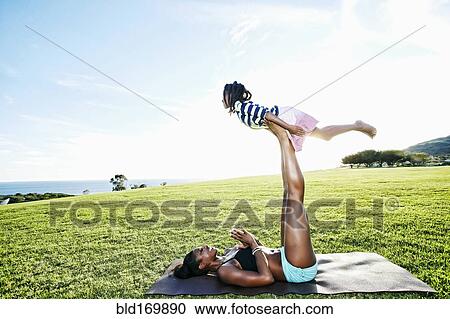 Stock Image - Mother holding daughter with legs in park. Fotosearch