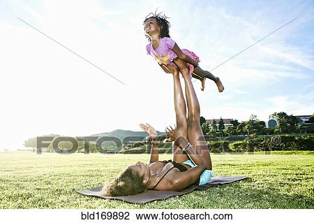 Stock Image - Mother holding daughter with legs in park. Fotosearch