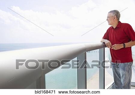 Stock Image - Older Black man overlooking ocean from balcony. Fotosearch