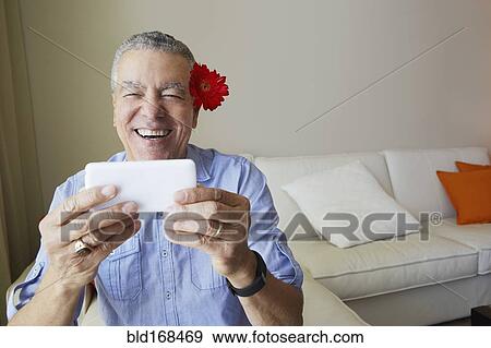 Stock Photo - Older Black man taking selfie with flower behind his ear. Fotosearch