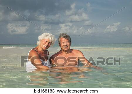 Stock Image - Older Caucasian couple swimming on beach. Fotosearch