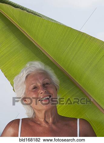 Stock Image - Older Caucasian woman standing under leaf. Fotosearch