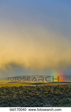 Stock Image - Rainbow and clouds over desert landscape. Fotosearch