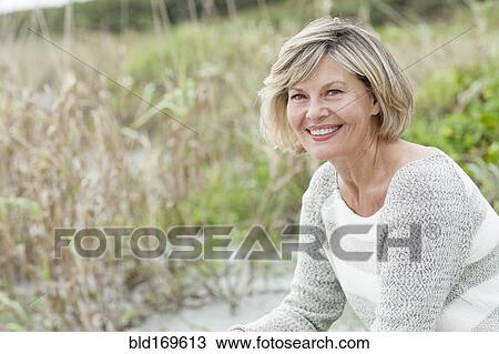 Stock Image - Smiling Caucasian woman sitting on beach. Fotosearch