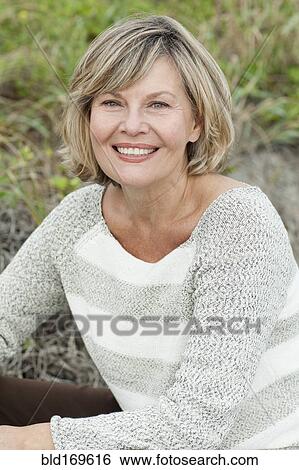 Stock Photograph - Smiling Caucasian woman sitting on beach. Fotosearch