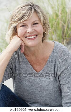 Stock Photography - Smiling Caucasian woman sitting on beach. Fotosearch
