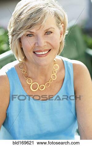 Stock Image - Smiling Caucasian woman sitting on park bench. Fotosearch