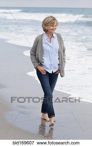 Stock Photo - Smiling Caucasian woman walking on beach. Fotosearch
