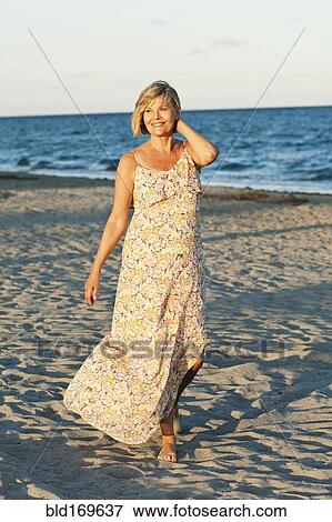 Stock Photo - Smiling Caucasian woman walking on beach. Fotosearch