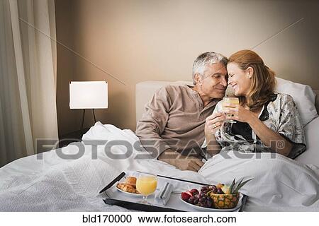 Stock Image - Smiling couple having breakfast in bed. Fotosearch
