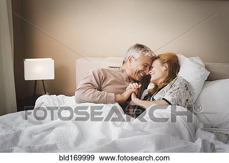 Stock Photo - Smiling couple holding hands on bed. Fotosearch