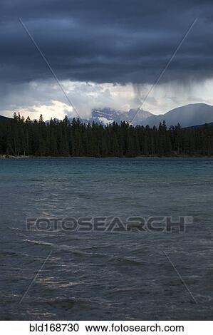 Stock Image - Storm clouds raining over lake. Fotosearch