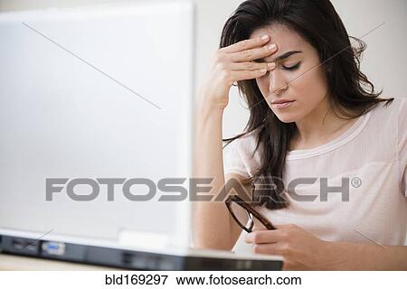 Stock Photo - Stressed woman rubbing her forehead at laptop. Fotosearch