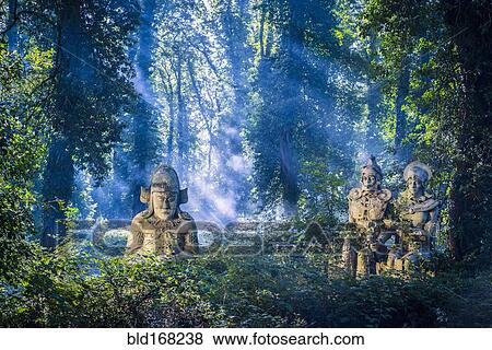 Stock Photo - Sunbeams on ancient statues in lush forest. Fotosearch