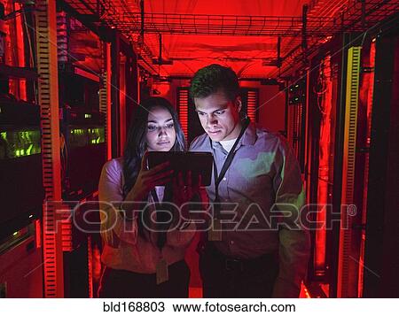 Stock Image - Technicians using digital tablet in server room. Fotosearch