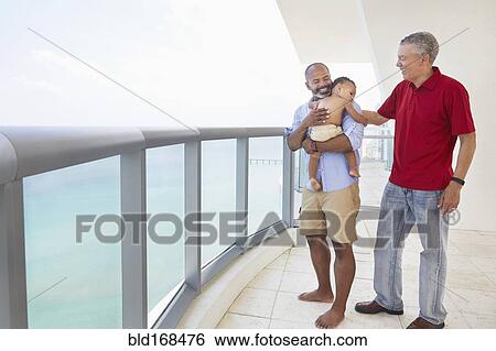 Stock Photograph - Three generations of men standing on balcony. Fotosearch