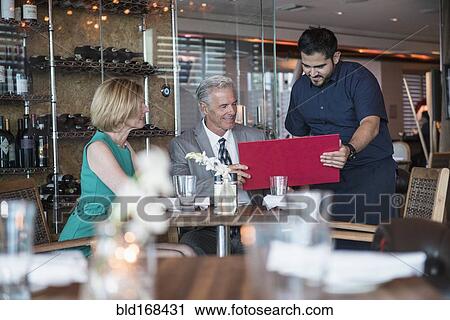 Waiter assisting couple with menu in restaurant View Large Photo Image Stock Image - Waiter assisting couple with menu in restaurant. Fotosearch