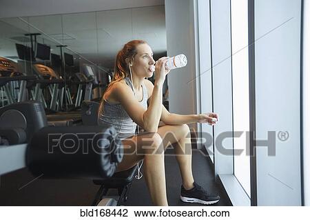Stock Image - Woman drinking water bottle in gym. Fotosearch