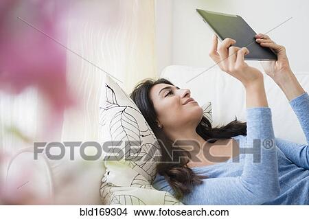 Picture - Woman using digital tablet on sofa. Fotosearch