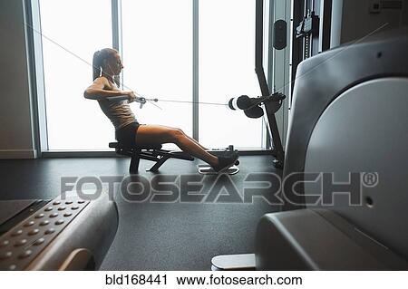 Stock Image - Woman using exercise machine in gym. Fotosearch