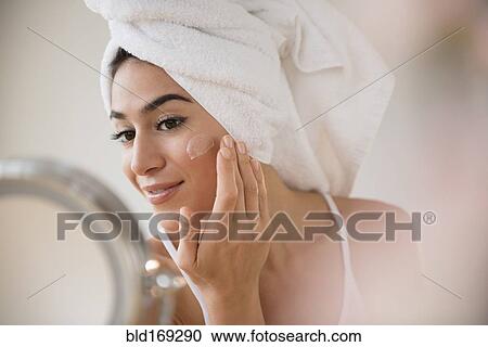 Stock Image - Woman with hair in towel rubbing lotion on face. Fotosearch