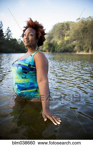 Stock Image - African American woman standing in rural lake. Fotosearch