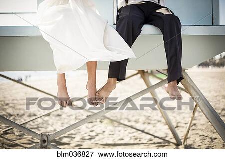 Stock Photo - Asian bride and groom sitting on lifeguard hut on beach. Fotosearch