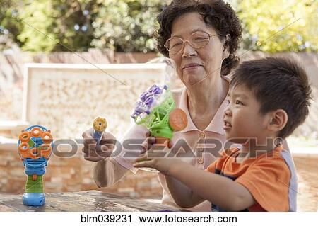 Stock Image - Asian grandmother and grandson blowing bubbles outdoors. Fotosearch