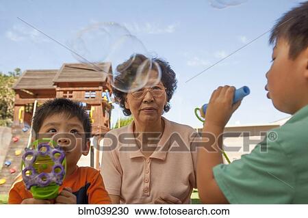 Asian grandmother and grandsons blowing bubbles outdoors View Large Photo Image Stock Image - Asian grandmother and grandsons blowing bubbles outdoors. Fotosearch